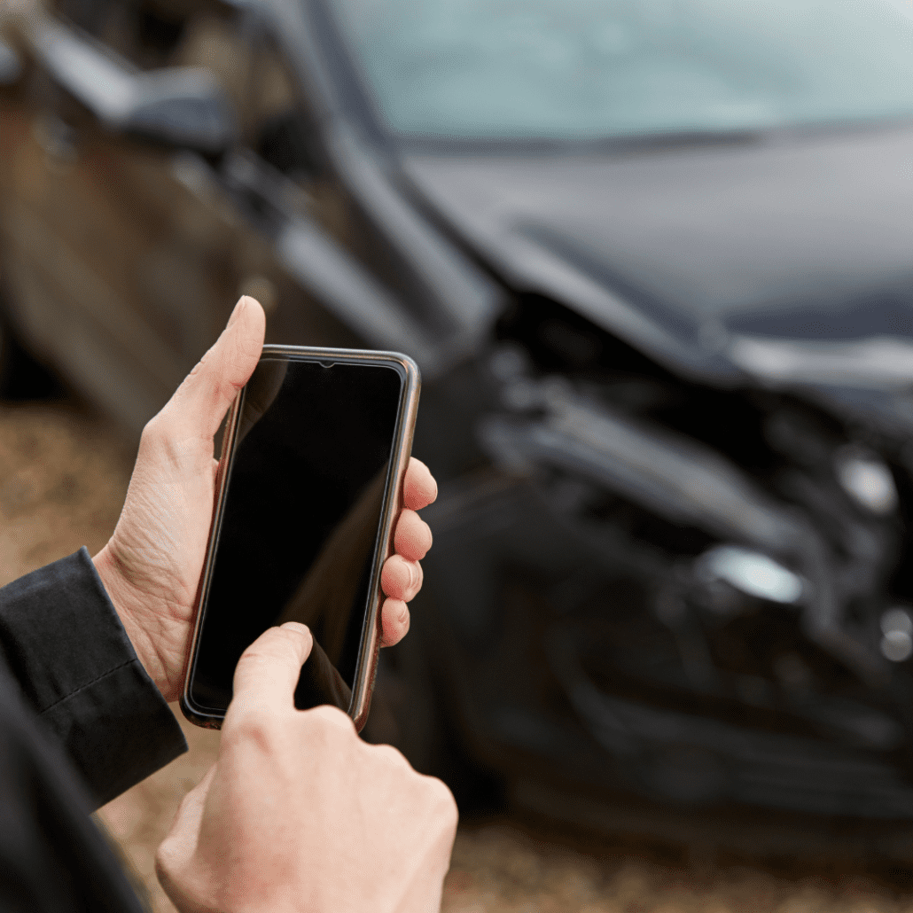 man holding his phone with a damaged car in the background